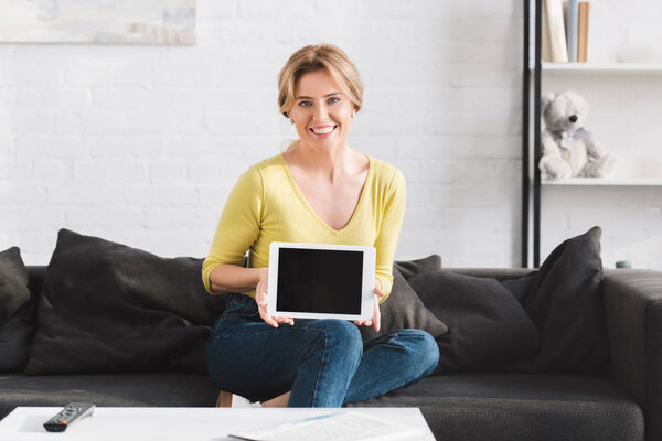 beautiful woman showing digital tablet with blank screen and smiling at camera 
