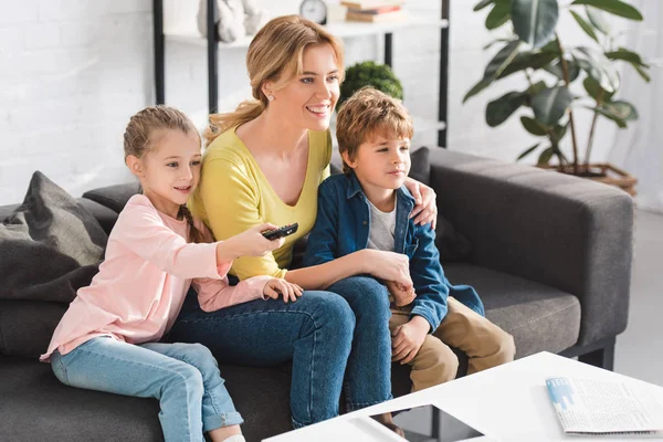 リモート コント ローラーを使用して 一緒にテレビを見ている子供たちが幸せな母とかわいい笑顔 — ストック写真