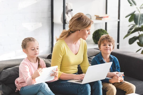 Madre Hermosos Niños Sentados Sofá Utilizando Dispositivos Digitales Casa —  Fotos de Stock