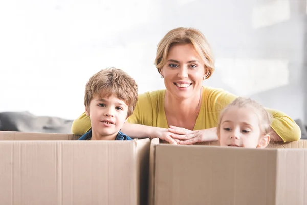 Feliz Madre Sonriendo Cámara Lindos Niños Pequeños Sentados Cajas Cartón — Foto de Stock