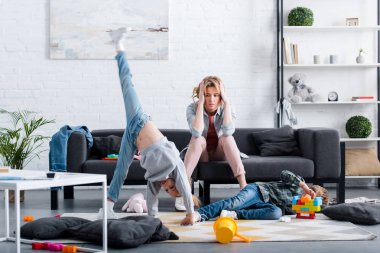 kanepede oturan ve evde oynarken yaramaz çocuklara bakarak yorgun anne 