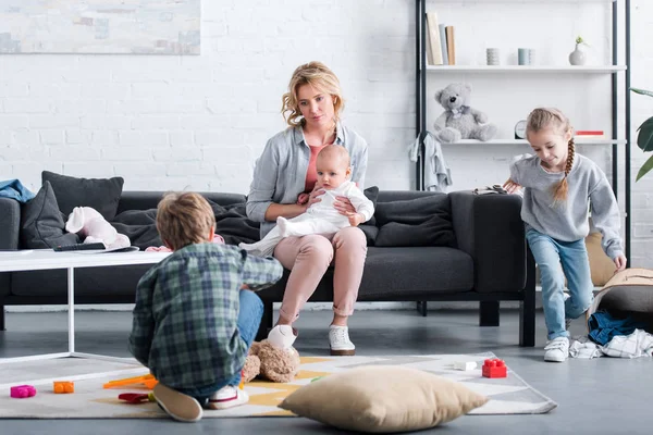 Tired Mother Infant Child Sitting Couch Looking Naughty Siblings Playing — Stock Photo, Image