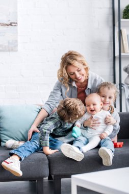 happy mother looking at three adorable children sitting on couch clipart