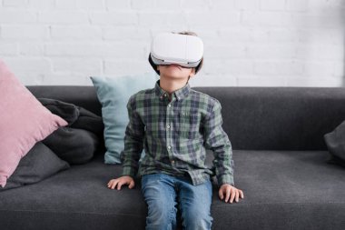 kanepede oturan ve evde sanal gerçeklik kulaklık kullanarak sevimli çocuk  