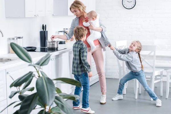 Mãe Cansada Segurando Criança Infantil Cozinhar Enquanto Crianças Impertinentes Brincando — Fotografia de Stock