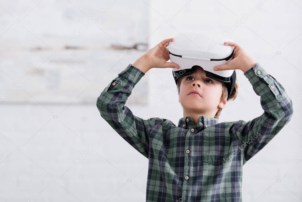 adorable boy using virtual reality headset and looking away at home