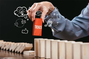 cropped view of woman picking red block with word 'trends' out of wooden bricks, icons on foreground clipart