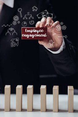 cropped view of woman holding red wooden brick with words 'employee engagement' isolated on black, icons on foreground clipart