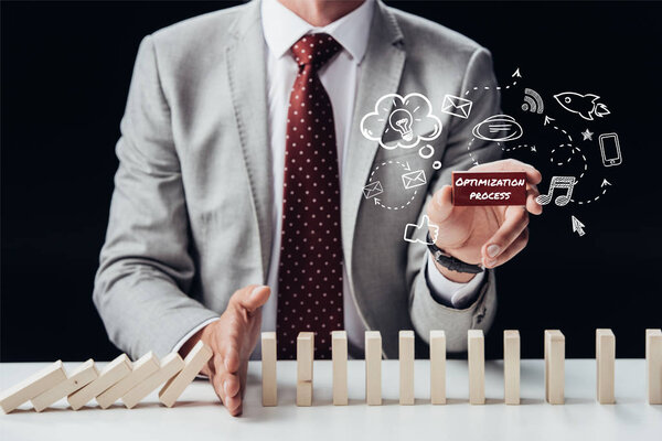 cropped view of businessman preventing wooden blocks from falling while holding brick with words 'optimization process', icons on foreground