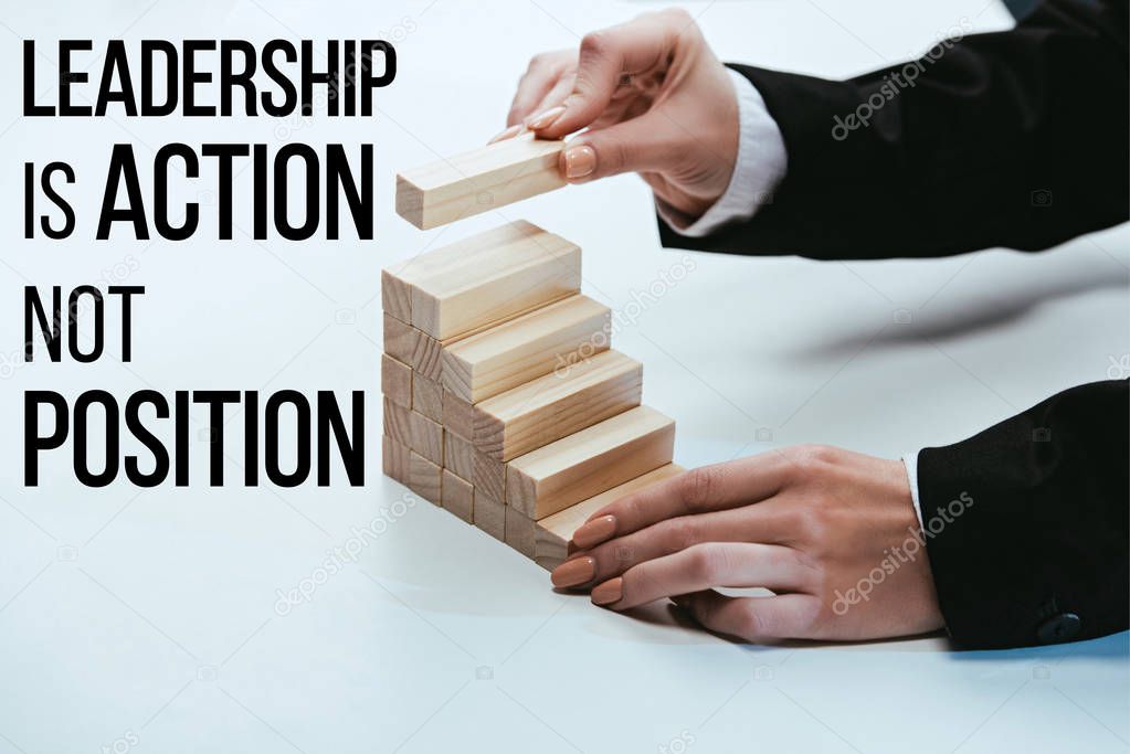 cropped view of woman building career ladder with wooden blocks, 'leadership is action not position' lettering on foreground