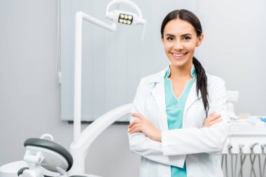 beautiful dentist standing with crossed arms in dental clinic clipart