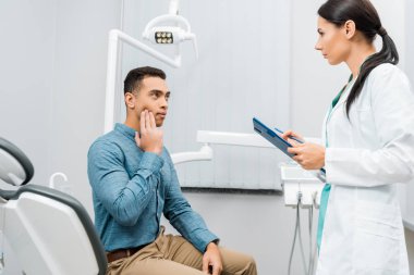 female dentist standing near  african american patient with toothache  clipart