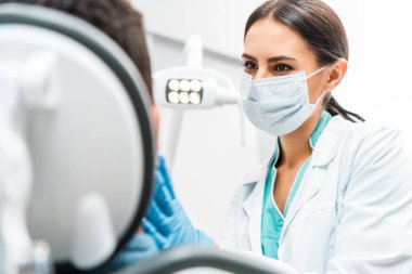 Diş Kliniği hastada bakarak maskeli kadın diş hekimi