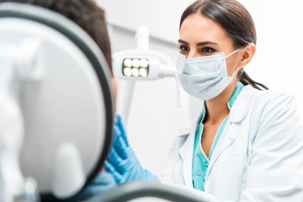 female dentist in mask looking at patient in dental clinic