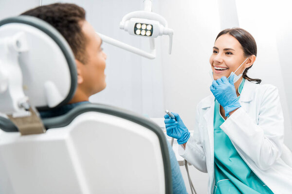 smiling female dentist holding drill near patient 