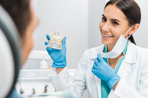 smiling female stomatologist showing dental jaw model with braces to patient 
