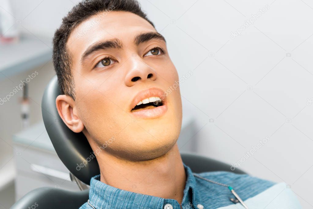close up of handsome african american man with open mouth in dental clinic 