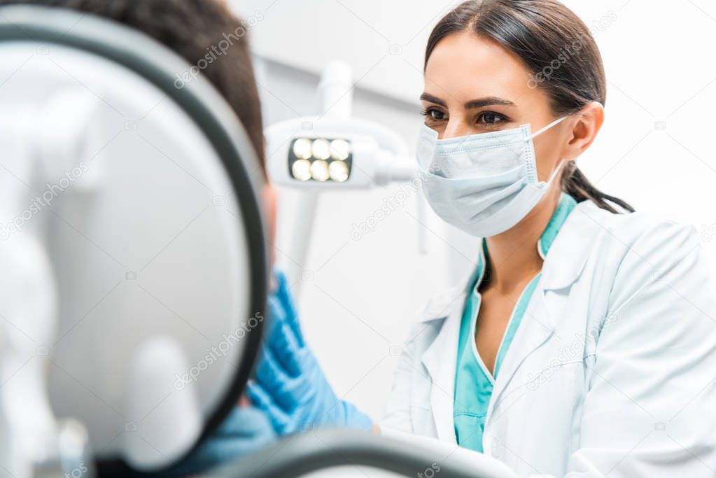 female dentist in mask looking at patient in dental clinic