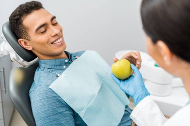 femaledentist giving apple to handsome african american patient  clipart