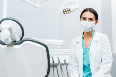 Beyaz önlük ve maske diş sandalye yakınındaki kadın diş hekimi 