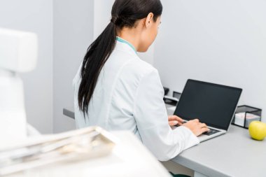 arkadan kadın doktor dizüstü bilgisayarda yazarak görünüşü 