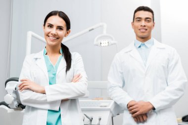 çapraz kolları olan beyaz önlük Afro-Amerikan iş arkadaşı ayakta neşeli kadın doktor 