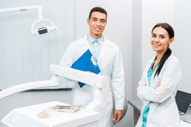 Pano yakınındaki çapraz kolları olan güzel iş arkadaşınız ile ayakta yakışıklı Afrikalı-Amerikalı doktor