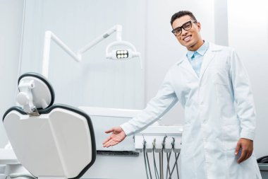 Afrika kökenli Amerikalı doktor diş kliniğinde sandalye gösterilen gülümseyen 