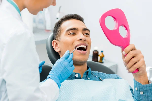 Dentista Mujer Sosteniendo Instrumento Médico Cerca Paciente Afroamericano Mirando Espejo —  Fotos de Stock