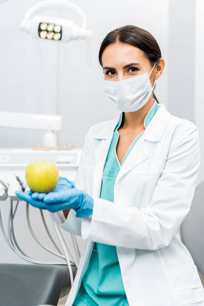 female stomatologist in white coat and mask holding apple 