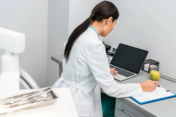 Doctor Femenino Usando Ordenador Portátil Con Pantalla Blanco Tomando Notas — Foto de Stock