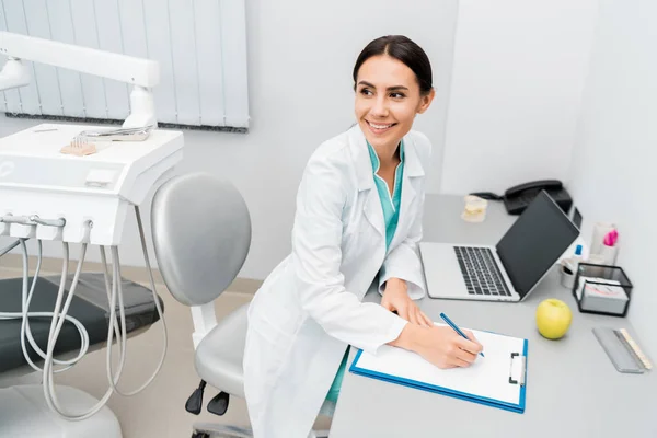 Médico Atraente Feminino Fazendo Anotações Perto Laptop — Fotografia de Stock