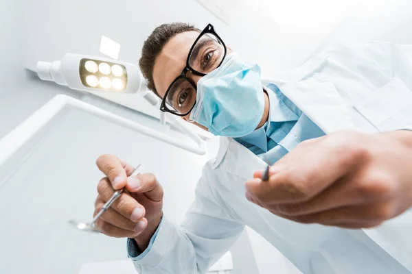 戴眼镜和面罩的男性牙医手里的牙科器械 — 图库照片