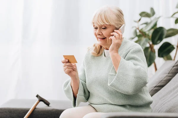 Sonriente Rubia Jubilada Mujer Mirando Tarjeta Crédito Mientras Habla Teléfono — Foto de Stock