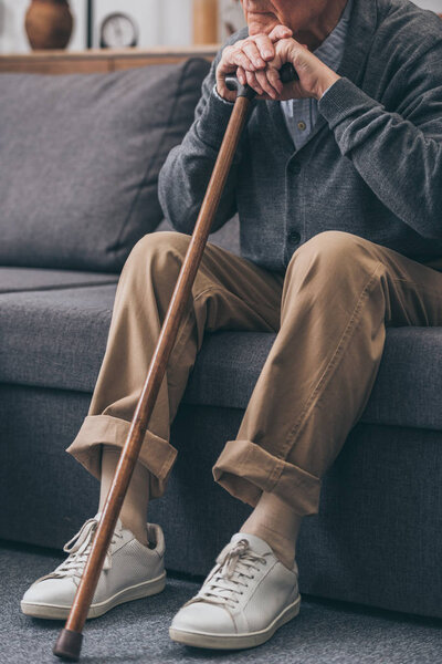 cropped view of male pensioner sitting on sofa with walking cane