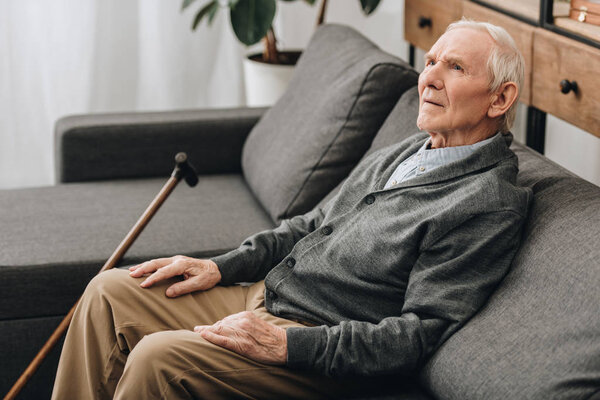 thoughtful pensioner with grey hair sitting on sofa 