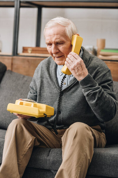 retired man using old phone while sitting on sofa