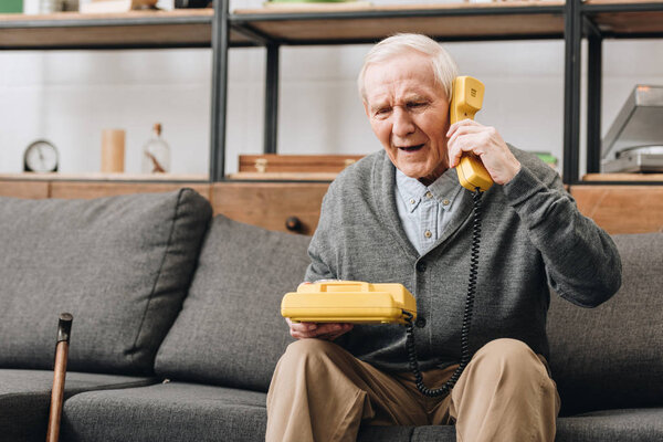 retired man talking on retro phone while sitting on sofa
