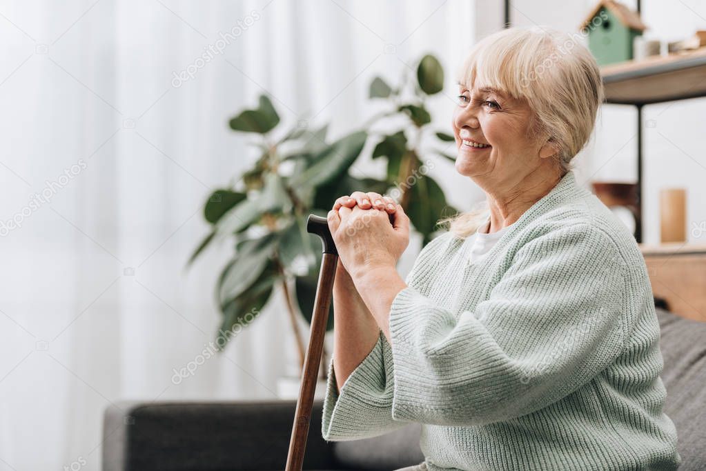 cheerful retired woman smiling and holding walking stick