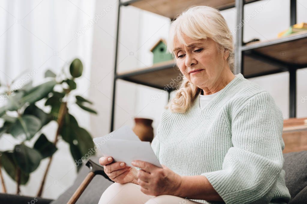 sad retired woman holding photos in living room