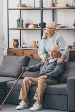 retired wife embrace sad senior husband sitting on sofa in living room  clipart