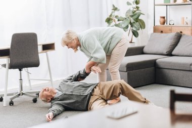 old woman helping to husband who falled down on floor clipart