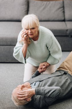 senior woman helping old husband who falled down on floor  clipart