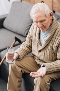senior man holding pills and glass of water and looking at hand clipart