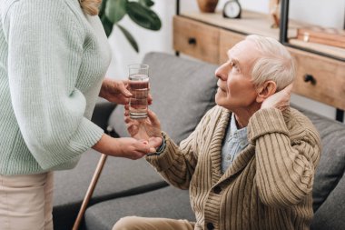 senior woman helping to old man with walking stick and giving pills  clipart