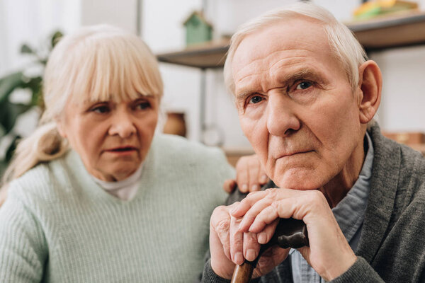 selective focus of sad pensioner sitting near retired wife at home 