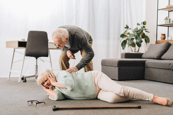 Unterstützender Pensionierter Ehemann Schaut Seniorin Boden Liegend Und Hält Kopf — Stockfoto