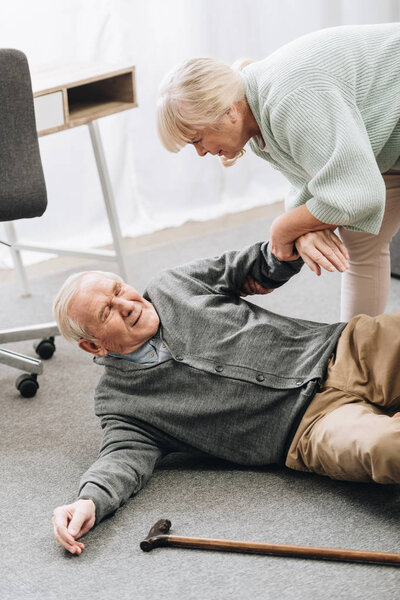 old woman helping to stand up husband who falled down on floor with walking stick