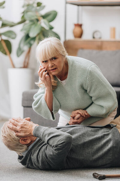 senior woman helping old man with walking stick and looking at camera