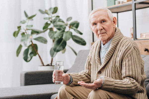 senior man holding pills and glass of water and looking at camera